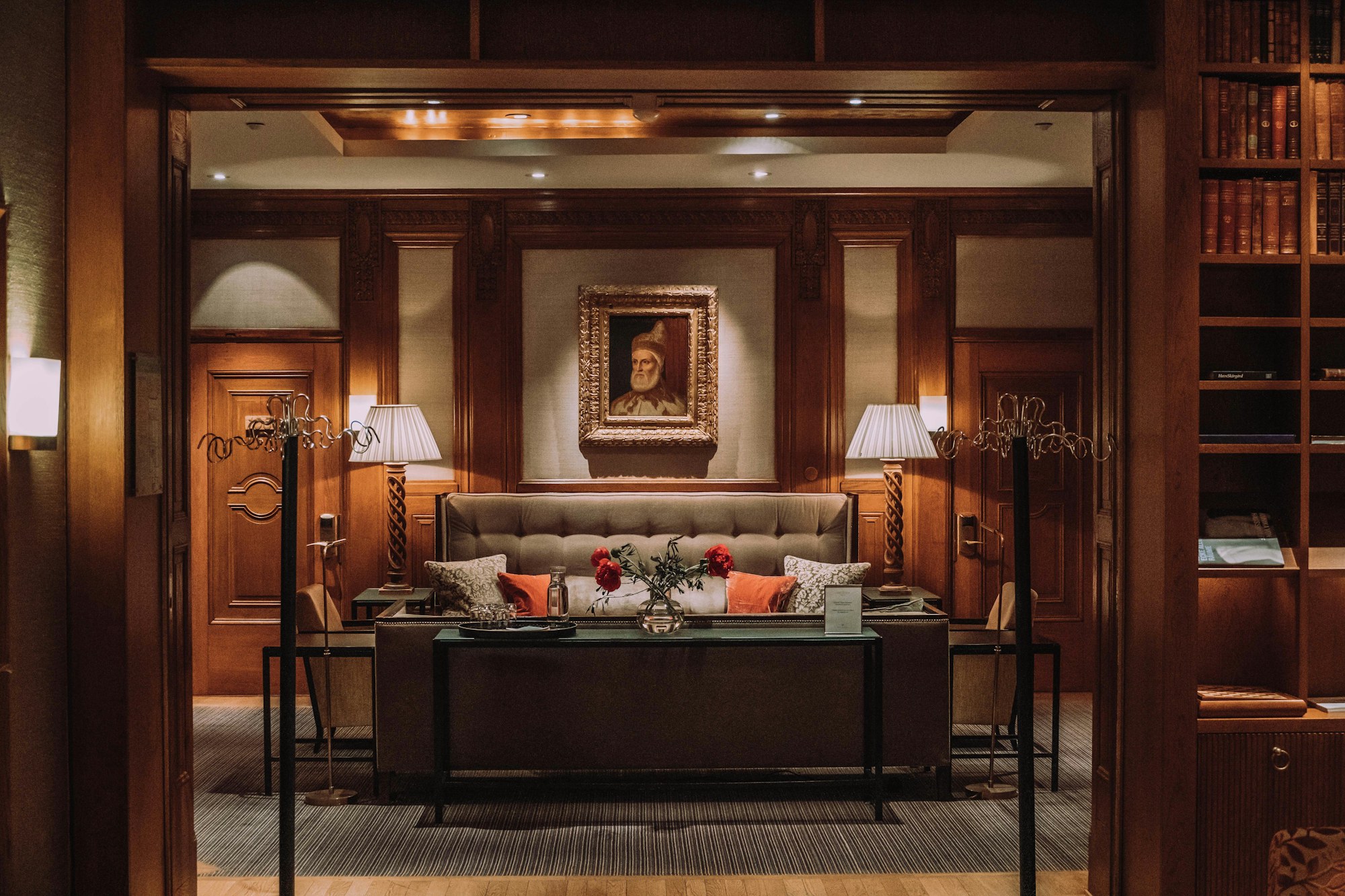 Wood-paneled townhouse library with a tufted settee, carved-wood lamps, and shelves of books